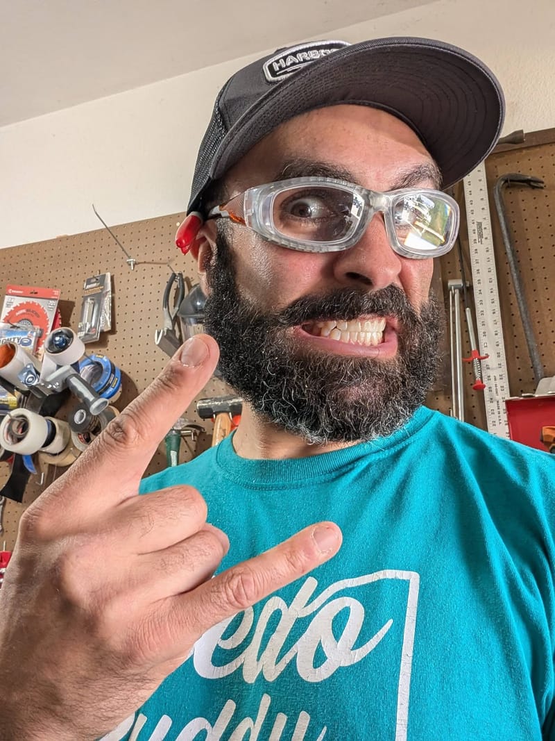Abe in a garage workshop wearing safety glasses, pulling a face at the camera.